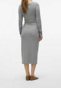 Långärmad, grå stickad klänning med en figurnära silhuett som når mitt på vaden, slät textur, i kombination med bruna slip-on skor.