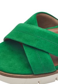 Sandalo verde in suede con cinturini incrociati, una fodera interna marrone e una suola in gomma bianca con finitura testurizzata.