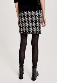 Sukně s houndstooth vzorem v černobílé barvě vyrobená z texturované látky, kombinovaná s černými punčochami a robustními kotníkovými botami.