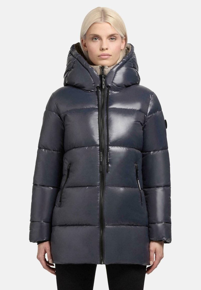 Gevoerde donkergrijze jas met een hoge kraag en een oversized capuchon. Beschikt over een rits aan de voorkant, zijzakken en een glanzende afwerking met doorgestikte secties.