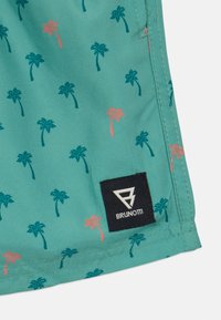 Pantaloni da bagno turchesi con piccoli motivi di palme in verde e corallo. Presentano un'etichetta di marca nera con logo bianco sull'orlo.