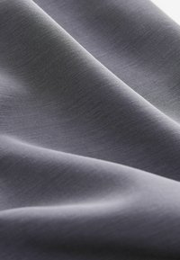 Grått tyg med en slät, matt yta som visar subtila veck och draperingar. Materialet verkar lätt och mjukt.