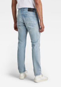 Ljusblå denimjeans med slim fit, femficksdesign och en svart läderlapp på midjan. Strukturerad tyg med måttlig blekning.