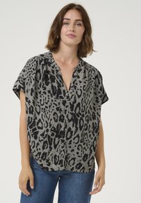 Blouse à manches courtes en tissu gris avec un motif léopard noir, dotée d'un décolleté en V et d'une coupe décontractée.