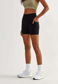 Black high-waisted shorts with a smooth texture and side pockets, paired with white athletic shoes and ribbed white socks.