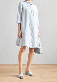 Lichtblauw gestreepte blouse jurk met kraag en zak, gecombineerd met lichtblauwe blokhak sandalen en een bijpassende handtas.