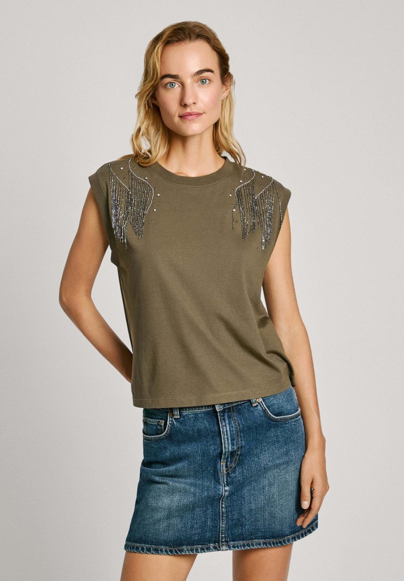 Alyvuogių žalia trumpų rankovių marškinėliai su karoliukais ir franžėmis ant pečių, derinami su mėlynu džinsiniu mini sijonu. Medvilnės mišinio audinys.