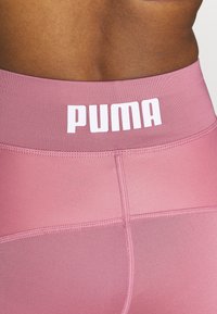 Leggings rosas con una textura suave, que presentan una cinturilla ancha con el logo "PUMA" en blanco y costuras cosidas para un detalle adicional.
