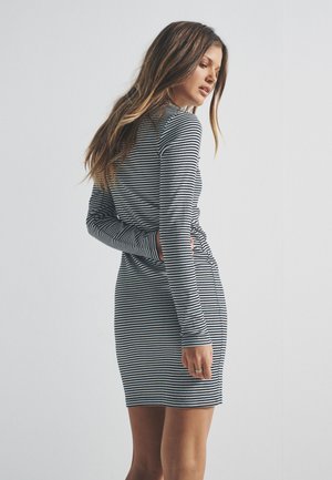 Robe à manches longues rayée noire et blanche, coupe ajustée, textile doux, longueur au genou, dotée d'un col rond et d'un détail discret sur le côté.