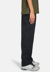 Pantalons droits noirs en coton, associés à des chaussures de sport argentées. La tenue présente un design simple et une coupe décontractée.