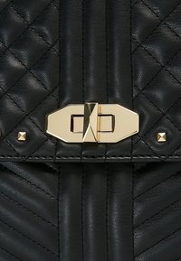 Svart läderhandväska med en quiltad design, guldtonad rektangulär låsöppning och metallnitar som accent. Texturerad yta genom hela väskan.