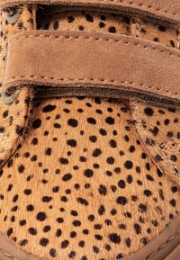 Scarpa in velcro marrone con macchie, caratterizzata da un upper in stampa animale testurizzata e una soffice fascetta in suede, con cuciture marroni e un design a punta arrotondata.