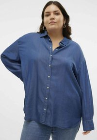 Camisa de mezclilla oscura de corte holgado, con mangas largas, cuello y cierre frontal de botones. Tejido suave con una textura sutil y un dobladillo curvado.