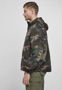 Camo-gepatroneerde hoodiejack in donkergroene en bruine tinten, met elastische manchetten en een ritszak aan de zijkant. Lichtgewicht stof.