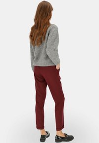 Szary, puszysty sweter; burgundowe, dopasowane spodnie; czarne, błyszczące loafersy z teksturowaną podeszwą; modelka lekko się obróciła, pokazując strój z tyłu.