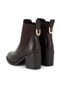 Brahmas brūni ādas potītes zābaki ar elastīgiem sānu paneļiem un zelta akcentiem. Blokveida papēži un gluda virsma. Apaļa pirksta forma.