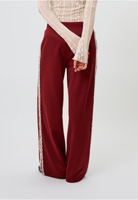 Platus kojas kelnės iš gilaus burgundiško audinio, su nėrinių apdaila šoniniuose kraštuose. Minkšta tekstūra ir elastinis juosmuo patogumui.