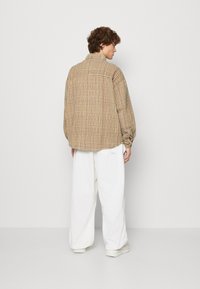 Brown checkered oversized jacket with soft texture, button cuffs, and a relaxed fit, paired with white wide-leg pants and white sneakers.