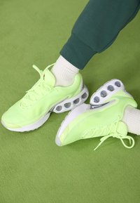 Neon zöld sportcipők hálós felsőrésszel, texturált részletekkel és egyedülálló fehér és szürke árnyalatú légpárnás rendszerrel.
