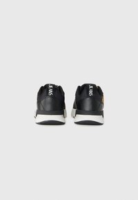 Baskets noires avec une finition en cuir lisse, semelle blanche et dos texturé. Présente l'inscription "JEANS" imprimée en blanc sur le talon.