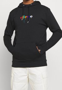 Sweat à capuche noir avec une poche avant. Présente un logo texte multicolore dégoulinant. Confectionné en tissu doux avec des poignets et un ourlet côtelés.