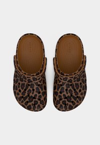 Ζευγάρι καφέ Crocs με μαύρο και σκούρο καφέ λεοπάρ σχέδιο και οπές αερισμού, απεικονιζόμενα από πάνω πάνω σε λευκό φόντο.