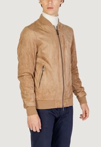 Chaqueta bomber de ante color beige con cremallera frontal, bolsillos laterales, puños acanalados y dobladillo. Textura suave y diseño aerodinámico.