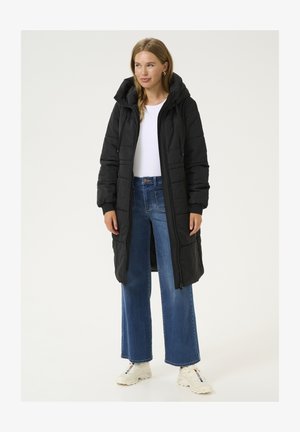 Manteau doudoune noir avec capuche, doté d'une fermeture éclair et de poignets élastiques, associé à un jeans bleu à jambes larges et des baskets blanches.