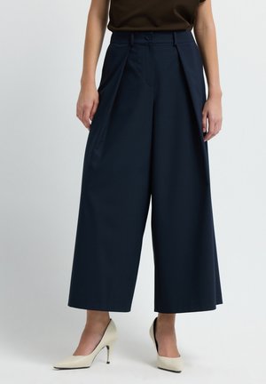 Navy wijd-uitlopende broeken met plooien, op maat gemaakte stof en een aansluitende taille. Gecombineerd met crèmekleurige puntige hakken. Glad textuur, minimale afwerking.