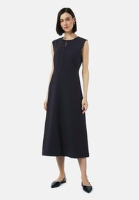 Robe sans manches navy avec un décolleté arrondi, un d�étail en trou de clé à l'avant et une silhouette fluide en A, associée à des ballerines noires.