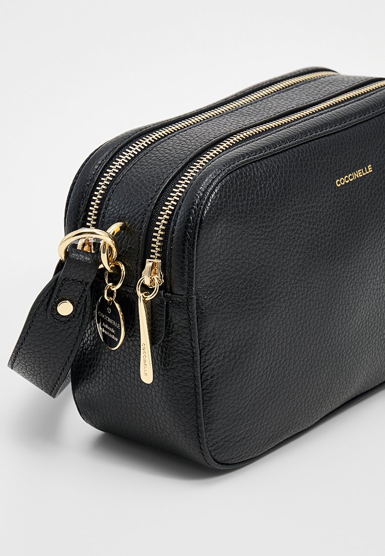 Trousse de maquillage en cuir noir texturé avec une double fermeture éclair, des accents en métal doré et une sangle détachable. Logo visible sur le côté.