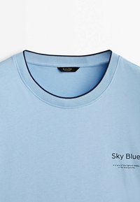 Himmelsblå bomulds T-shirt med rund hals. Har en marineblå ribbet krave og trykt tekst på forsiden. Glat overflade, afslappet design.