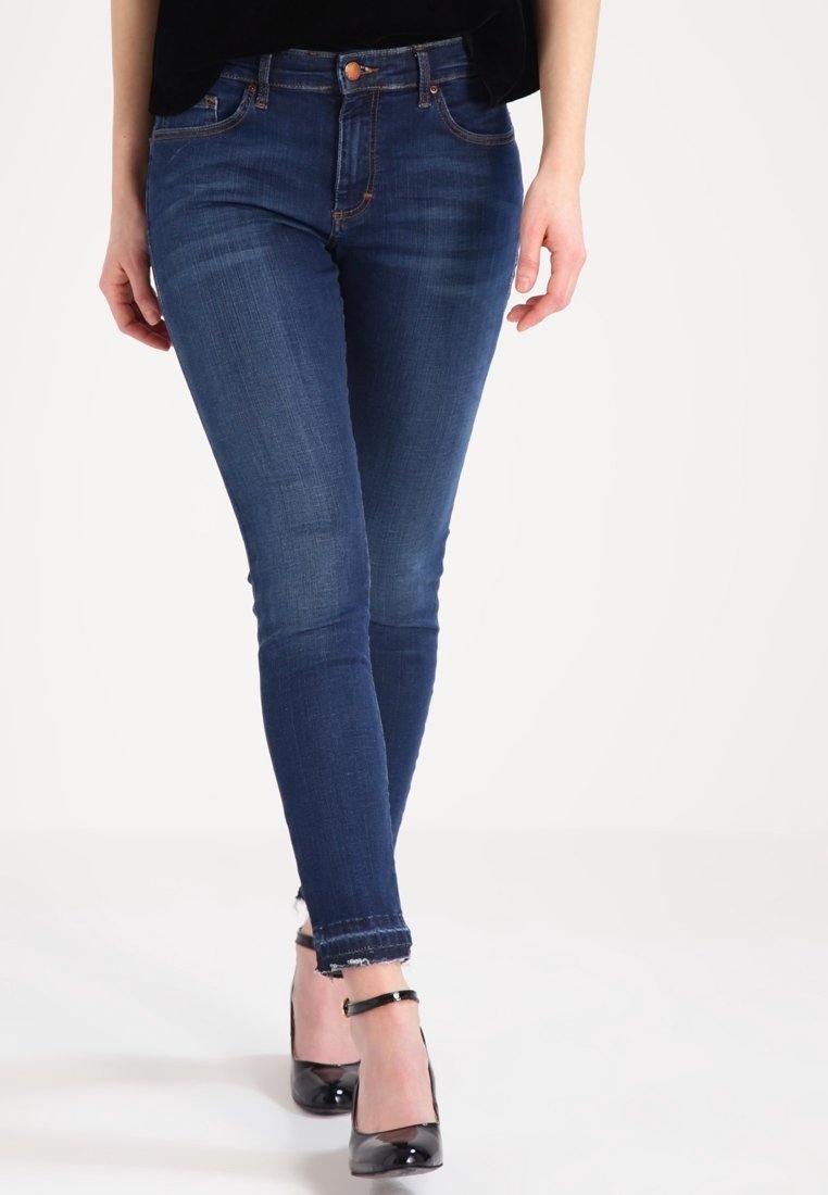 Smalblå jeans med en mjuk denimtextur, som har midjehöjd, minimal sömnad och en fransig fåll. Kombinerade med svarta högklackade skor.