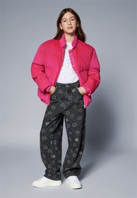 Roza jakna s pufovima, bijela majica, sivi hlače s uzorkom nasmijanih lica i bijeli tenisice. Glatka tekstura s oversized krojem.