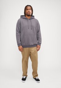 Grå hettegenser med justerbare snorene, kengurulomme, ribbede mansjetter, sammen med lyse brune rette bukser og svarte sneakers.