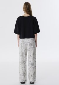 Zwarte cropped t-shirt en grijze patroonkorte broek met handgeschreven tekst en grafische ontwerpen, gladde stof en een relaxte pasvorm.