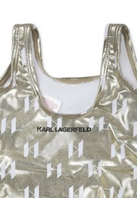 Débardeur métallique doré avec une finition texturée et des motifs géométriques blancs. Affiche "KARL LAGERFELD" en lettres noires sur le devant.