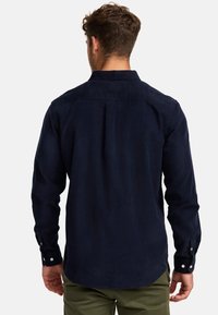 Mörkblå, långärmad kordskjorta med ett vikat krage, knappärmar och ett ryggveck. Har en slät textur och en strukturerad passform.