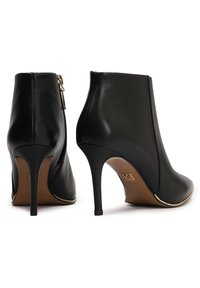Stivali alla caviglia in pelle nera con un design elegante, punta affusolata, tacco a stiletto alto e dettagli dorati lungo la suola e la cerniera.