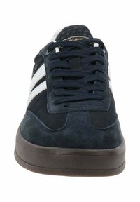 Sneaker scuro in suede navy con strisce bianche, dotato di linguetta testurizzata, lacci piatti e suola in gomma marrone.