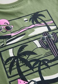 Grøn bomulds T-shirt med et grafisk design af en pink is, palmer, en kaktus og en solnedgang i sort og hvid.