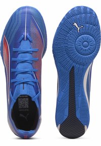 Blaue Sportschuhe mit roten und weißen Akzenten, Schnürsenkel gebunden, einer zeigt die Draufsicht, der andere die texturierte Sohle mit Puma-Logo.