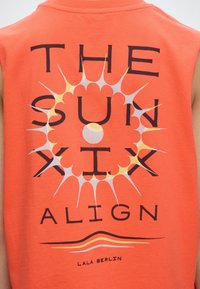 Πορτοκαλί αμάνικη μπλούζα με στυλιζαρισμένο γραφικό ήλιο και το κείμενο «THE SUN SIX ALIGN» και το όνομα της μάρκας «LALA BERLIN» στην πλάτη.