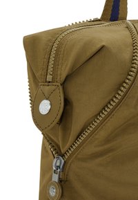 Sac à dos en nylon marron avec une finition texturée, comportant une fermeture éclair visible, des accents en métal et une étiquette en cuir avec un logo.