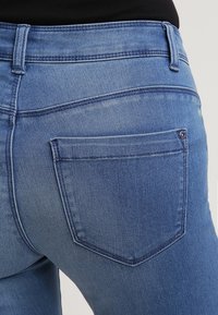 Modré džíny z denimu s těsným střihem, obsahující klasickou zadní kapsu a jemné vyblednutí. Hladká textura a standardní detaily šití.