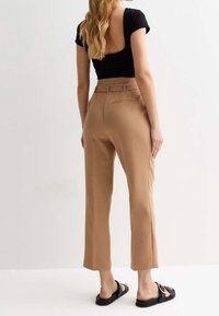Beige hooggesneden pantalon met een rechte pijp, voorzien van een achterzak en een ceintuurlus, gecombineerd met een zwarte strakke top.