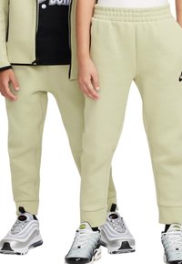 Pantaloni della tuta verde chiaro con vita elasticizzata, gambe affusolate e dettagli con logo Nike, abbinati a scarpe da ginnastica grigie. Tessuto morbido e testurizzato.