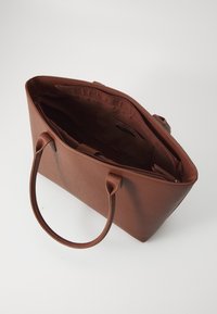 Sac fourre-tout en cuir marron avec des poignées incurvées, de forme rectangulaire et un dessus zippé. L'intérieur dispose d'un revêtement doux et d'une poche latérale.