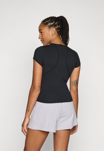 Top atletico nero a maniche corte, con un design aderente e dettagli di cucitura curvati, abbinato a pantaloni corti grigio chiaro.