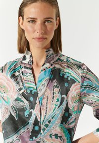Bunt bedruckte Bluse aus leichtem Stoff. Sie hat einen Mandarin-Kragen, kurze Ärmel und eine Mischung aus rosa, blau und schwarz.